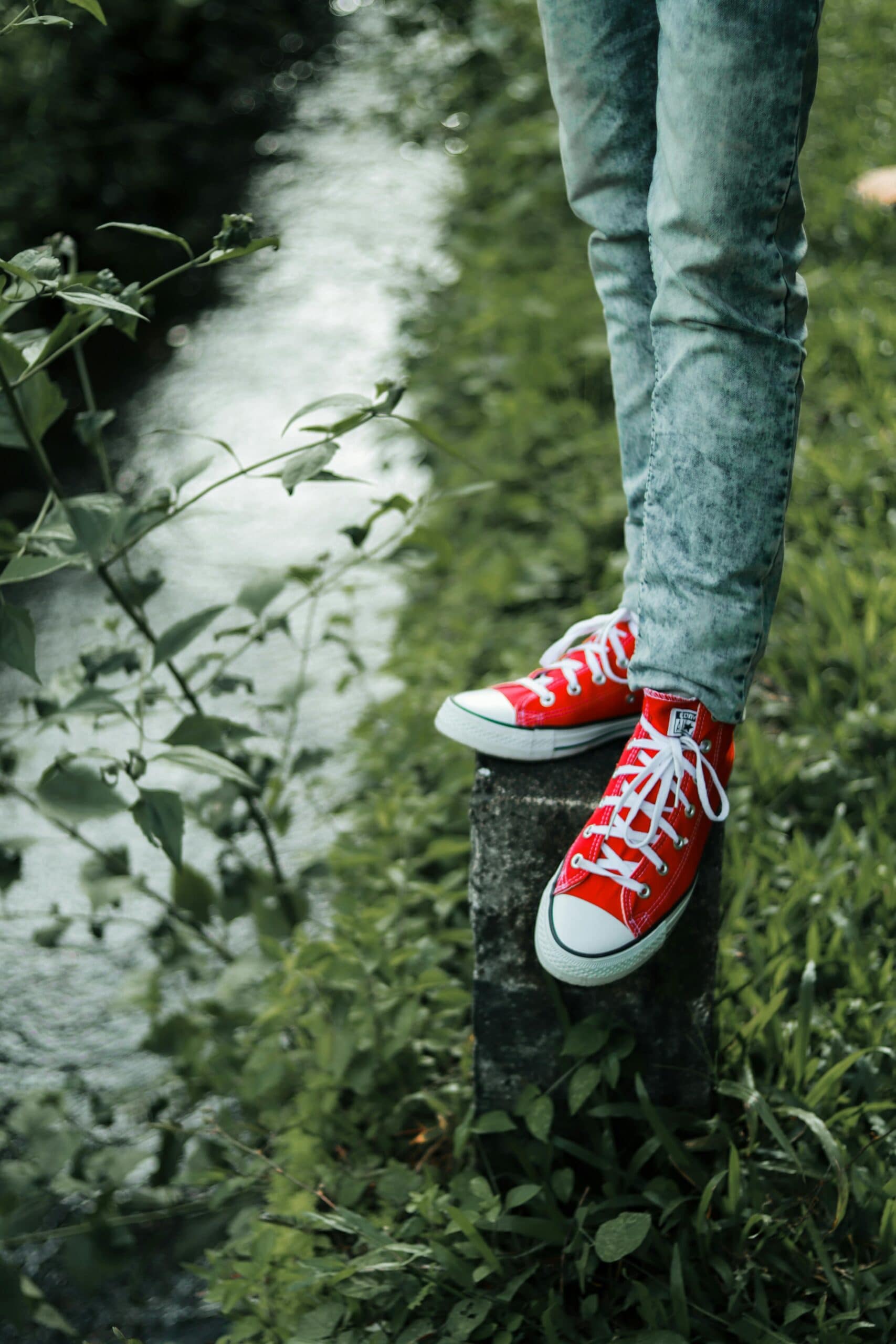 Person wearing red sneakers standing on a concrete post near a stream.