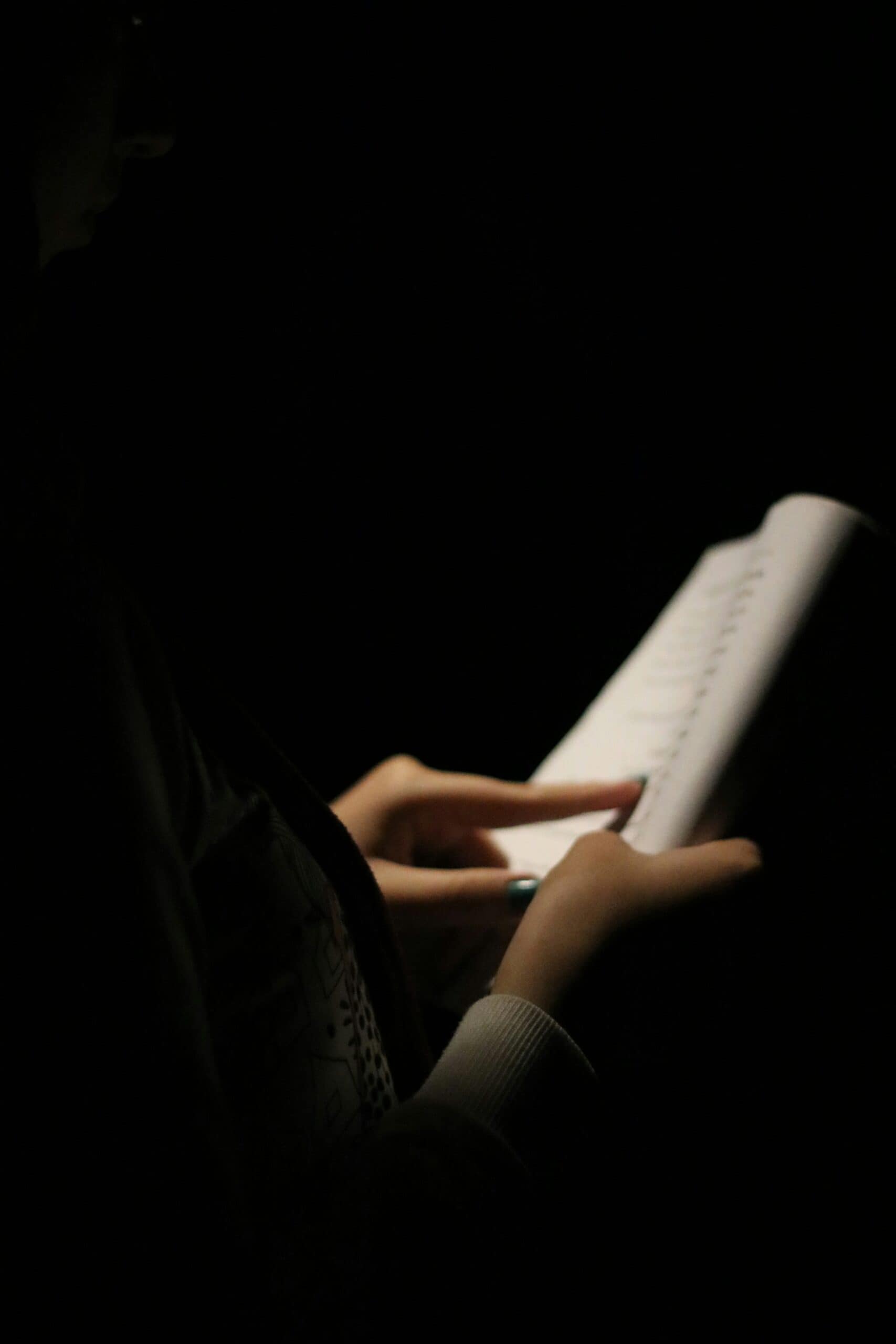 Person reading a book in a dark room, illuminated by the book's light.