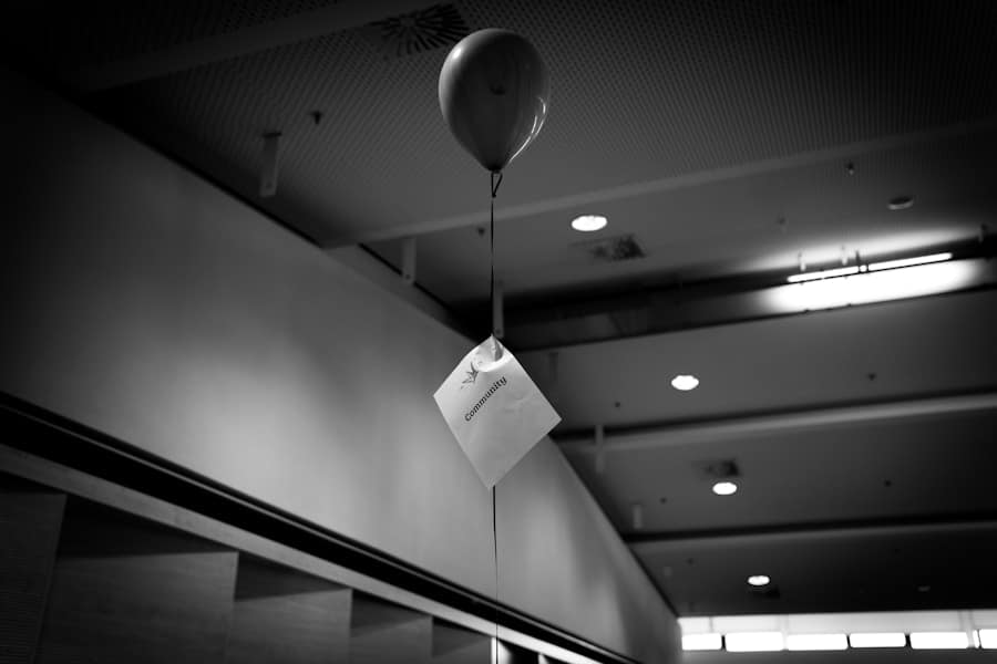 A black and white image of a helium balloon with a paper attached, floating indoors.
